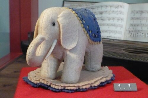 Grauer Filzelefant von Steiff mit blauer Decke auf dem Rücken als Nadelkissen