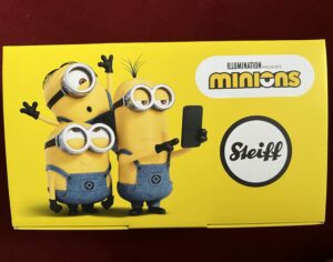 Luxusplüsch- Gelber Minion Karton mit drei Minion-Figuren, Steiff Logo und Text Illumnination presents Minions